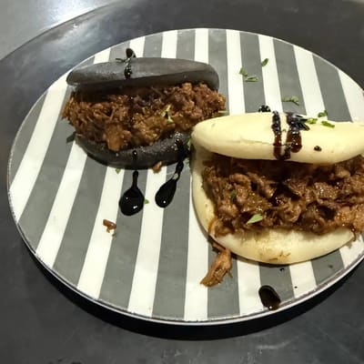 Dos panecillos al vapor, uno blanco y otro negro, rellenos de carne deshilachada con salsa oscura