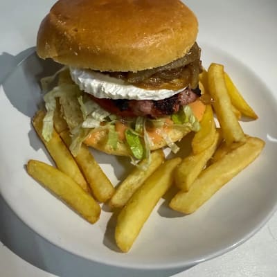 Hamburguesa en pan brioche con queso cremoso fundido, cebolla dorada y lechuga, rodeada de patatas fritas