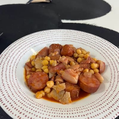 Guiso caldoso en plato hondo, con garbanzos, rodajas de chorizo y tacos de panceta
