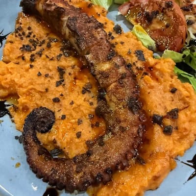 Tentáculo a la plancha con especias sobre un puré anaranjado, con tomate asado al lado