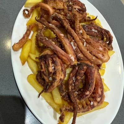 Tentáculos dorados en la freidora sobre una cama de patatas, con sal gruesa por encima